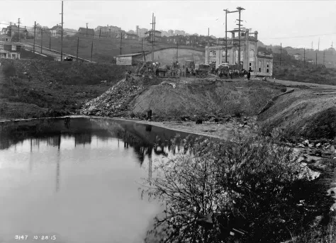 A shoreline dump beside Lake Union, Seattle, in 1915 — refuse tipped down the bank to the waterline below hillside houses.
