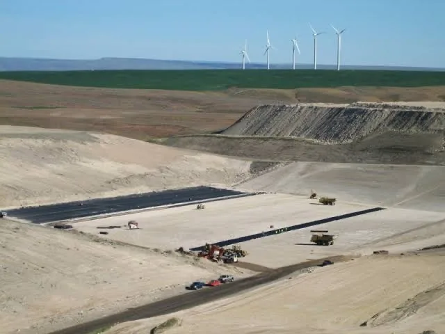 An engineered cell under construction at the Columbia Ridge Landfill, its liner exposed beneath wind turbines on the ridge.